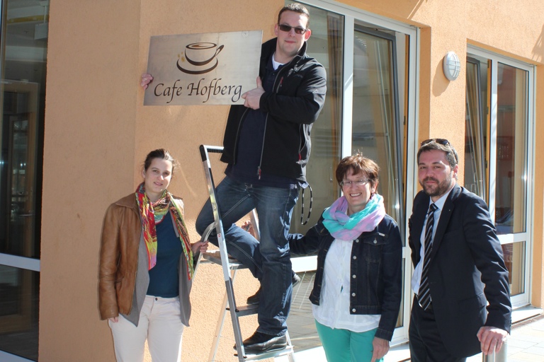 Das neue Namensschild des Café Hofberg installiert der neue Pächter Marcus Andre. Mit im Bild Architektin Stefanie Schauer (von links), die bisherige Pächterin Vroni Reil und Bürgermeister Thomas Herker. Foto: Steinbüchler